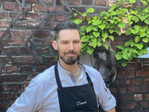 a man wearing an apron standing in front of a brick wall at Wellings Romantik Hotel zur Linde in Moers