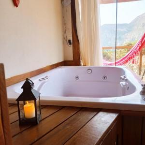 a bath tub in a bathroom with a candle and a window at Chalé com Jacuzzi vista para Pico da Lapinha in Santana do Riacho +102 photos