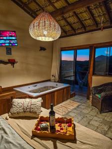 a bedroom with a tub and a table with a bottle of wine at Chalé com Jacuzzi vista para Pico da Lapinha in Santana do Riacho