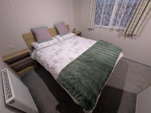 a bedroom with a bed with a green and white blanket at Seascape Caravan in Kinmel Bay +24 photos