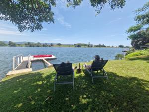 a person sitting in chairs next to a boat on a lake at Tweed River Waterfront Cottage in Murwillumbah