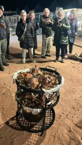 a group of people taking pictures of a grill with chickens at Shaheen Camp Wadi rum in Wadi Rum