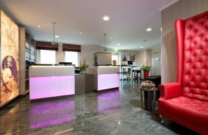 a living room with a red chair and a kitchen at Leonardo Hotel Nürnberg in Nuremberg