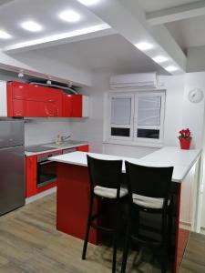 a kitchen with red cabinets and a counter with two chairs at Centro apartman 3 in Pančevo +5 photos