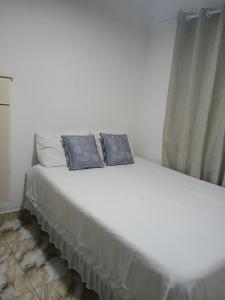 a white bed with two blue pillows on it at ElRancho Suites in Itaparica