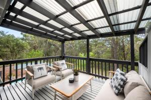 a screened porch with a couch and chairs on a deck at Blenheim Beach Retreat in Vincentia