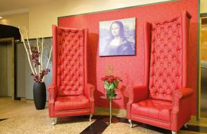 a room with two red chairs and a portrait of a woman at Leonardo Hotel Munich Arabellapark in Munich