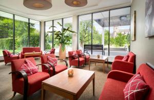 a waiting room with red chairs and tables and windows at Leonardo Hotel Mönchengladbach in Mönchengladbach