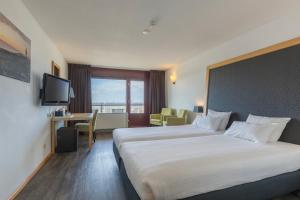 a hotel room with two beds and a television at Leonardo Hotel IJmuiden Seaport Beach in IJmuiden