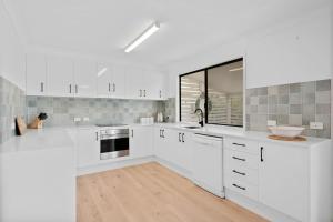 a white kitchen with white cabinets and a sink at Baileys Beach House in East Ballina +9 photos