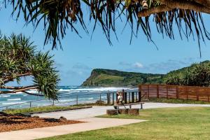 a bench sitting on a sidewalk looking at the ocean at Sun Soaked Lennox Village in Lennox Head