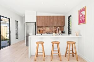 a kitchen with white countertops and wooden stools at Blue Ash Studio in Lennox Head +2 photos