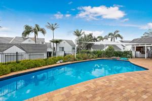 a swimming pool in front of a house with palm trees at Quarterdeck 18 in Lennox Head