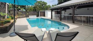 a swimming pool with two chairs and an umbrella at La Maison des Hôtes in Saint-Joseph