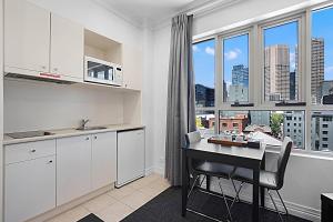 a kitchen with white cabinets and a desk with a window at Comfort Apartments Melbourne Central in Melbourne