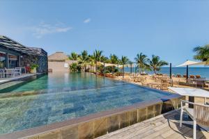 an infinity pool at a resort with chairs and umbrellas at Beachfront sea view apartment in Petite Case Noyale