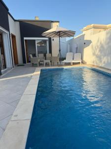a swimming pool with an umbrella next to a house at Villa alnaser in Awlād ‘Umar