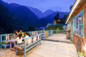 a group of people sitting at tables on a balcony with mountains at havana stays in Jibhi +10 photos