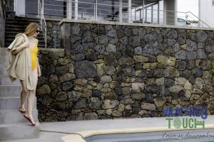 a woman standing next to a stone wall at Sunset Pool House in Feteira