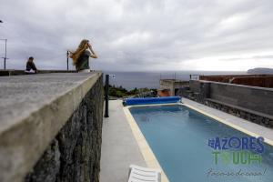 a woman standing on a ledge next to a swimming pool at Sunset Pool House T1 in Feteira