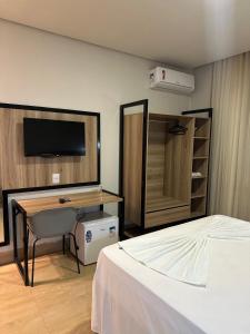 a bedroom with a bed and a desk and a television at Hotel Oscar Gold Janaúba in Janaúba