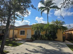 a yellow house with palm trees in front of it at Cozy Green Apartment in Homestead