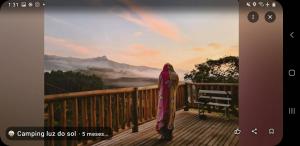 a woman standing on a wooden balcony with a painting at Camping luz do sol in Aiuruoca