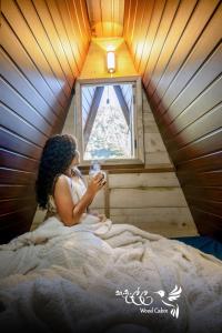 a woman sitting in bed in a room with a window at Kedella wood cabin in Nuwara Eliya