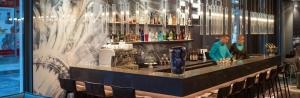 a woman standing behind a bar in a restaurant at Motel One Leipzig-Nikolaikirche in Leipzig