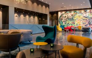 a lobby with colorful chairs and tables and a large mural at Motel One Leipzig-Post in Leipzig