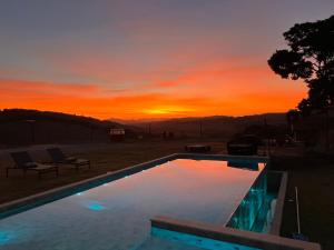 a sunset over a swimming pool with the sun setting at Olivas Eco Chalé in Pouso Alto