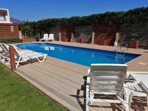 a swimming pool with white chairs next to at Cabañas Biancomoro Olmue in Olmué +11 photos