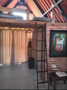 a room with a ladder and a television and a painting of a guitar at Chalé amora Analândia in Analândia