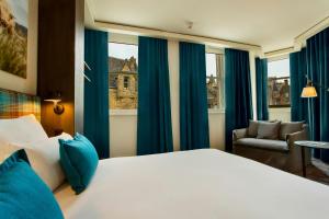 a bedroom with a bed and a chair and windows at Motel One Edinburgh-Royal in Edinburgh +27 photos