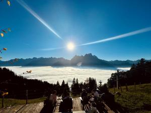 a group of people sitting on a bench watching the sun rise over clouds at Berggasthaus Eggberge - Boutique Mountain Hotel - Access via Cablecar in Altdorf