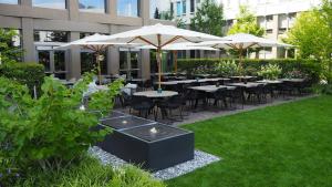 a group of tables and umbrellas in a garden at Motel One München-Campus in Munich
