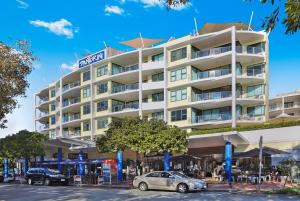 a large white building with cars parked in front of it at Santorini Twin Waters in Mudjimba