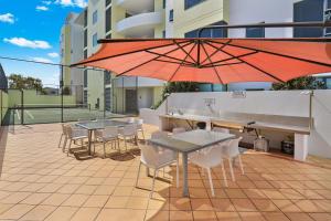 a patio with tables and chairs and an umbrella at Santorini Twin Waters in Mudjimba