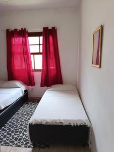 a bedroom with two beds and a window with red curtains at Cantinho da vovó Sol in Cabo Frio
