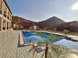 a swimming pool next to a building with a mountain at Orchard Hills Resorts in Pushkar