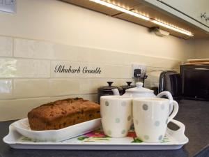 a tray with a cake and two cups on a counter at Wells Cottage in Hook Norton