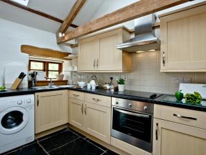 a kitchen with wooden cabinets and a washer and dryer at The Smithy in Chulmleigh