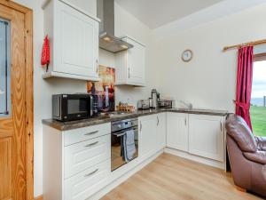a kitchen with white cabinets and a microwave at The Byre Mey in Scarfskerry