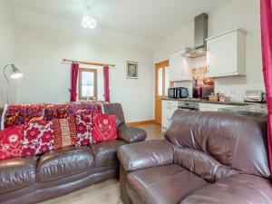 a living room with a leather couch and a kitchen at The Byre Mey in Scarfskerry