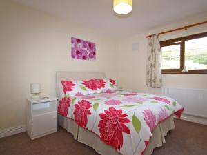 a bedroom with a bed with a floral bedspread and a window at Springer Cottage in Llanstephan