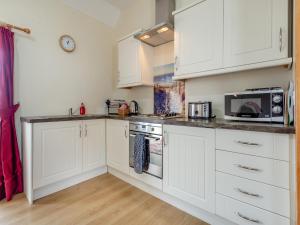 a white kitchen with white cabinets and a microwave at The Stable Mey in Scarfskerry +10 photos