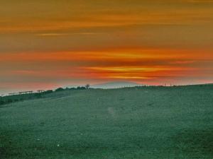 a sunset over a field with a mountain in the background at Halliday Hill Cottage in Dalton +3 photos