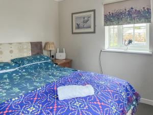 a bedroom with a bed with a blue comforter and a window at Heron's Lodge in Llanarthney