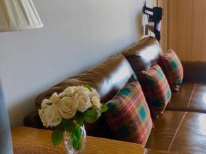 a leather couch with a vase of flowers on a table at Clarinnes Cottage in Rowardennan