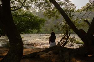 a woman sitting on a tree branch in front of a river at Pollachi Riverhouse, A CGH Earth Saha experience in Pollāchi